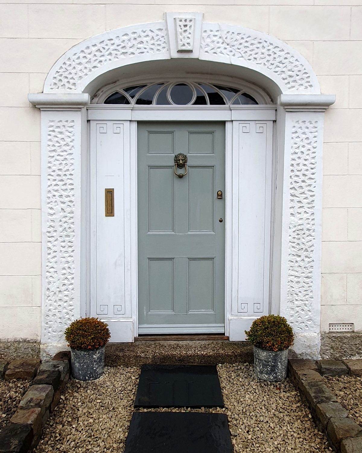 A pale grey panelled front door framed by an ornate white surround