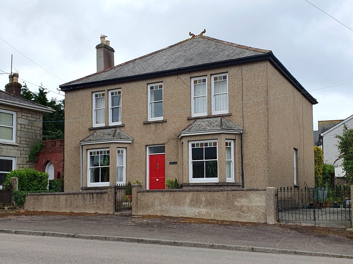 A detached home with a red front door behind a walled front garden